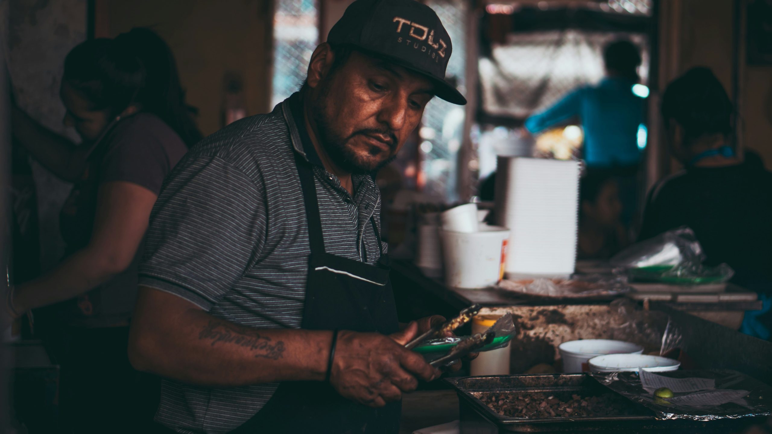 Hombre migrante trabajando en una cocina profesional con delantal.
